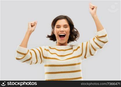 emotion, expression and success concept - happy smiling young woman in striped pullover celebrating triumph over grey background. happy young woman in pullover celebrating success
