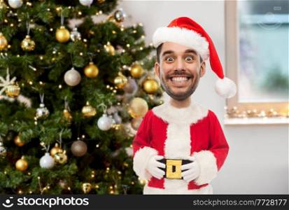 emotion, expression and winter holiday concept - happy smiling young man in santa claus costume over christmas tree on home background  funny cartoon style character with big head . smiling man in santa costume over christmas tree