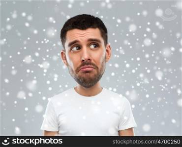 emotion, facial expression, winter, christmas and people concept - sad young man in white t-shirt looking up over snow on gray background (funny cartoon style character with big head)