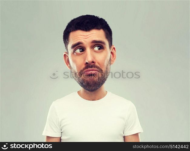emotion, facial expressions and people concept - sad young man in white t-shirt over gray background looking up (funny cartoon style character with big head). unhappy young man over gray background