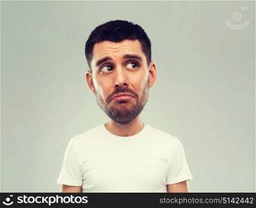 emotion, facial expressions and people concept - sad young man in white t-shirt over gray background looking up (funny cartoon style character with big head). unhappy young man over gray background