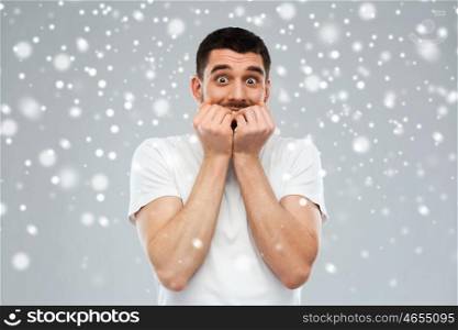 emotion, fear, winter, christmas and people concept - scared man in white t-shirt over snow on gray background