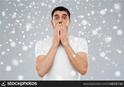emotion, fear, winter, christmas and people concept - scared man in white t-shirt over snow on gray background