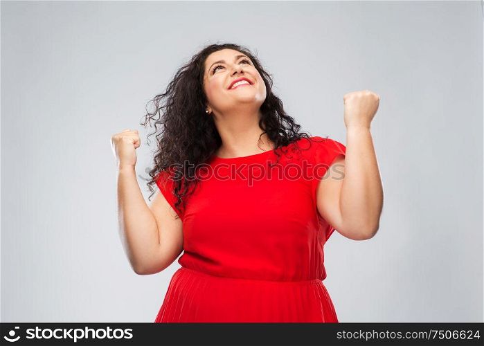 emotion, gesture and success concept - happy woman in red dress looking up and making fist pump over grey background. happy woman in red dress celebrating success