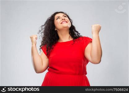 emotion, gesture and success concept - happy woman in red dress looking up and making fist pump over grey background. happy woman in red dress celebrating success
