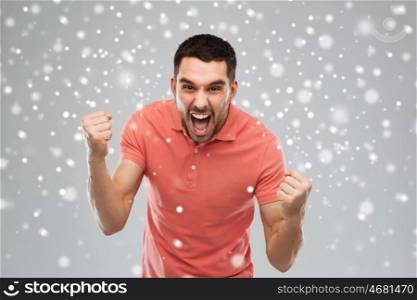 emotion, gesture, winter, christmas and people concept - angry young man holding fists over snow on gray background