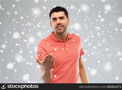 emotion, gesture, winter, christmas and people concept - arguing angry man proving something over snow on gray background