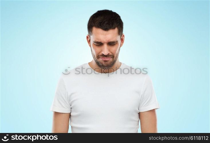 emotion, sadness and people concept - unhappy young man over blue background