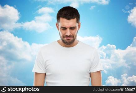emotion, sadness and people concept - unhappy young man over blue sky and clouds background