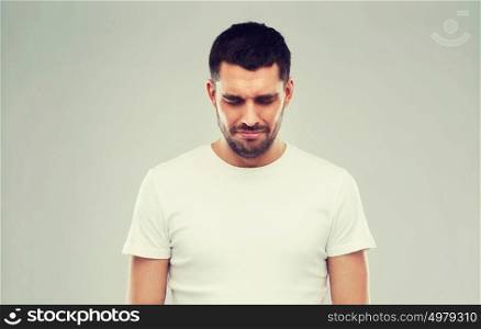 emotion, sadness and people concept - unhappy young man over gray background. unhappy young man over gray background