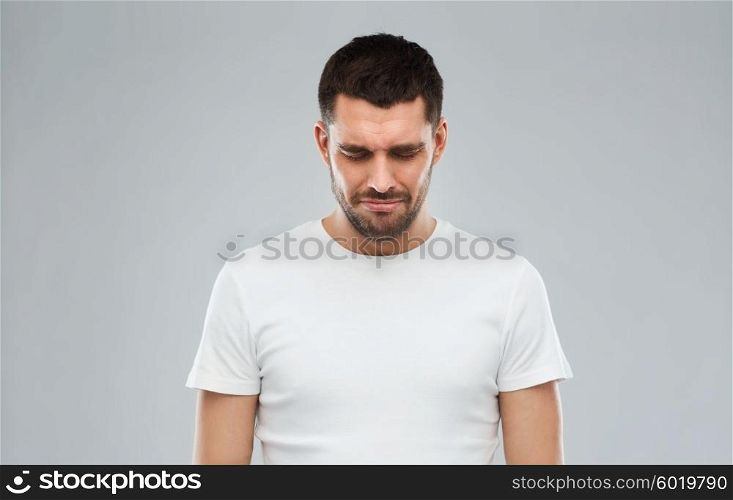 emotion, sadness and people concept - unhappy young man over gray background