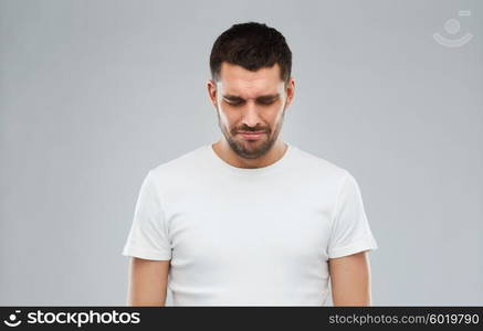 emotion, sadness and people concept - unhappy young man over gray background