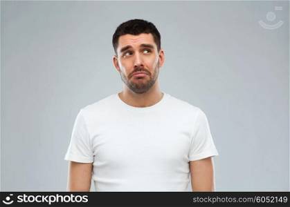 emotion, sadness and people concept - unhappy young man over gray background