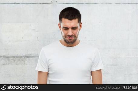 emotion, sadness and people concept - unhappy young man over gray wall background
