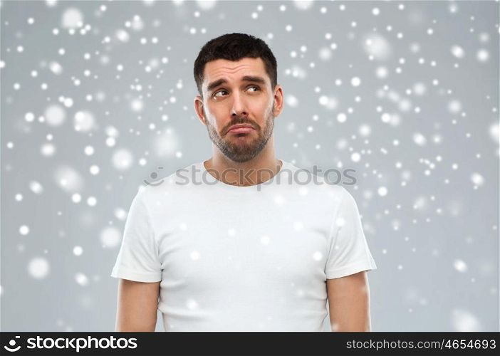 emotion, sadness, winter, christmas and people concept - unhappy young man over snow on gray background
