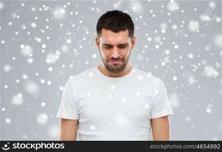emotion, sadness, winter, christmas and people concept - unhappy young man over snow on gray background