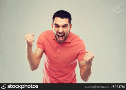 emotion, success, gesture and people concept - happy young man celebrating victory over gray background. happy man celebrating victory over gray background