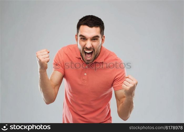 emotion, success, gesture and people concept - happy young man celebrating victory over gray background