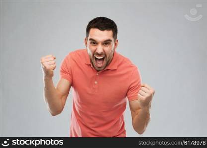 emotion, success, gesture and people concept - happy young man celebrating victory over gray background