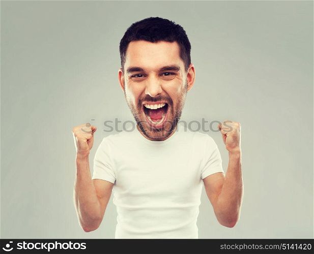 emotion, success, gesture and people concept - young man celebrating victory and screaming over gray background (funny cartoon style character with big head). young man celebrating victory over gray