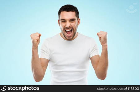 emotion, success, gesture and people concept - young man celebrating victory over blue background