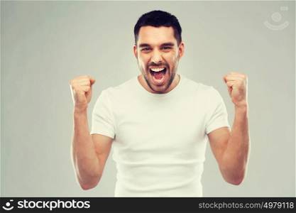 emotion, success, gesture and people concept - young man celebrating victory over gray background. young man celebrating victory over gray