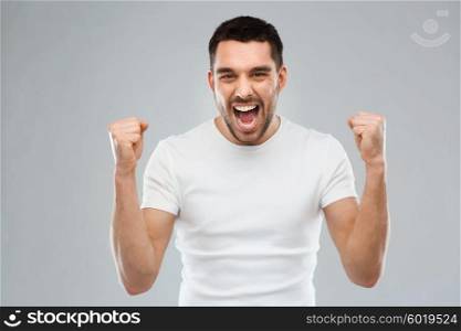 emotion, success, gesture and people concept - young man celebrating victory over gray background