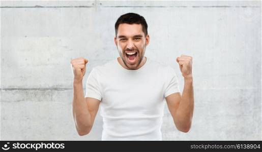 emotion, success, gesture and people concept - young man celebrating victory over gray stone wall background