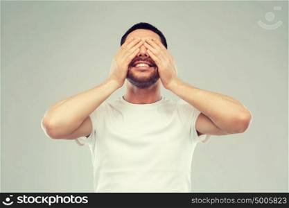 emotion, vision and people concept - smiling man closing his eyes with hands over gray background. smiling man closing his eyes over gray background