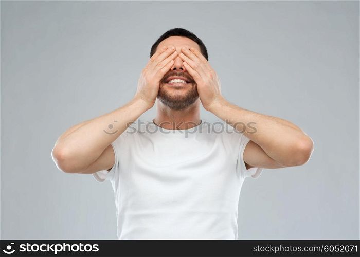 emotion, vision and people concept - smiling man closing his eyes with hands over gray background