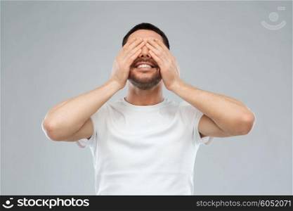 emotion, vision and people concept - smiling man closing his eyes with hands over gray background