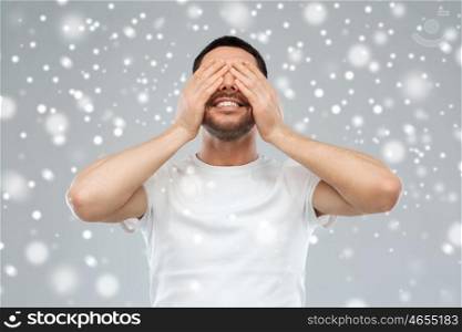 emotion, vision, winter, christmas and people concept - smiling man closing his eyes with hands over snow on gray background