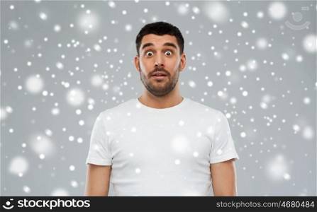 emotion, winter, christmas and people concept - scared man in white t-shirt over snow on gray background