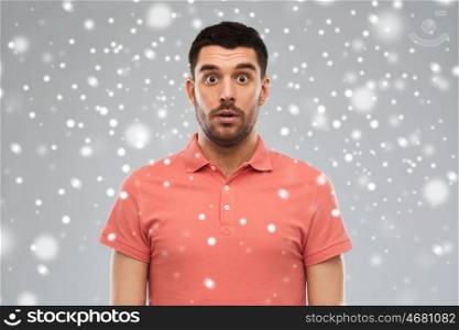 emotion, winter, christmas and people concept - surprised man in polo t-shirt over snow on gray background