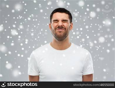 emotion, winter, christmas and people concept - young man screwing up his face over snow on gray background
