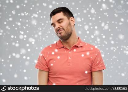 emotion, winter, christmas and people concept - young wrying man over snow on gray background