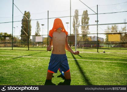 Emotional boy soccer player with t-shirt on head rejoicing goal or win showing yes gesture at stadium. Emotional boy soccer player with t-shirt on head rejoicing goal or win
