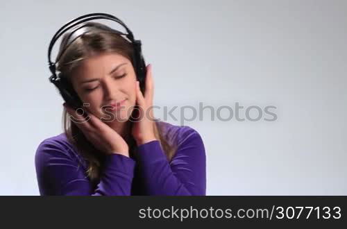 Emotional brunette woman with earphones listening music on white. Cheerful girl holding headphones with both hands, swaying along with the song, looking at the camera ,smiling playfully and blowing kiss while enjoying her music.