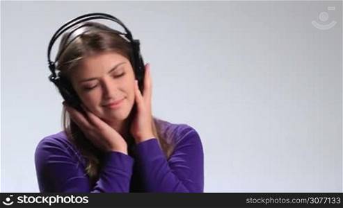 Emotional brunette woman with earphones listening music on white. Cheerful girl holding headphones with both hands, swaying along with the song, looking at the camera ,smiling playfully and blowing kiss while enjoying her music.