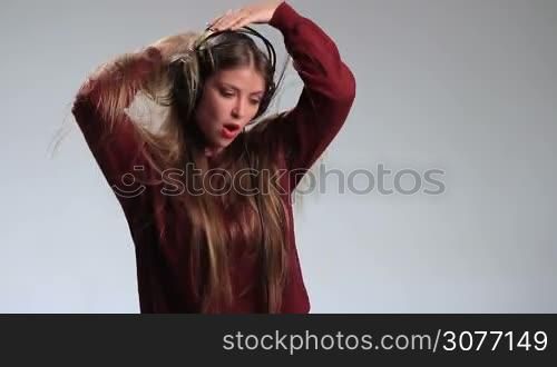 Emotional hipster girl in headphones enjoying her favorite music and dancing on white. Excited attractive woman in positive playful emotion listening music in headphones, playing with her amazing long hair, swinging to the beat and smiling cheerfuly.
