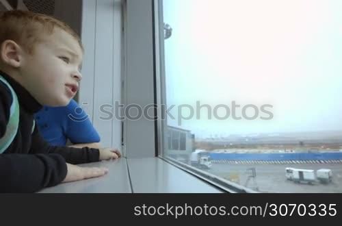Emotional little boy and young mother looking out the window at airport and pointing at something
