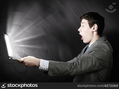 Emotional man using laptop. Young man looking in laptop screen with shock