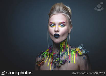 Emotional portrait of a young girl with creative makeup and colorful butterflies on her shoulders. Young girl with creative makeup with butterflies