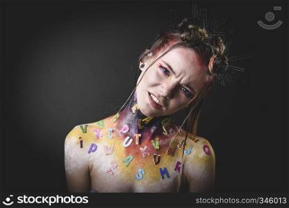 Emotional portrait of a young girl with creative makeup and colorful letters on her shoulders. Young girl with creative alphabet makeup