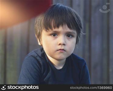 Emotional portrait of caucasian kid with thinking face with sunlight shining on his face, Upset little boy sitting alone in the park, Toddler with bored face looking out deep in thought.