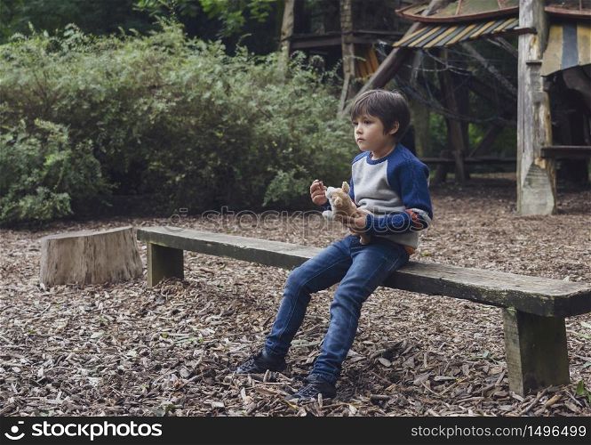 Emotional portrait of Lonely kid hugging dog toy sitting alone in the playground, Sad child sitting with his toy with looking deep in through, little boy playing alone with thinking face.