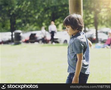 Emotional portrait of sad boy playing alone in playground with blurry car park background, Lonely Orphan child playing on his own, Dramatic portrait lost kid looking down with thinking face