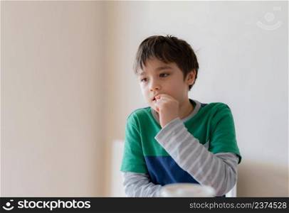 Emotional portrait young boy looking out deep in thought while eating nut, Cinematic portrait Child sitting alone with thinking face, Kid relaxing at home.