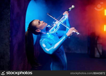 Emotional pretty woman artist playing violin in neon light and haze over loft industrial studio background. Emotional pretty woman artist playing violin in neon light and haze