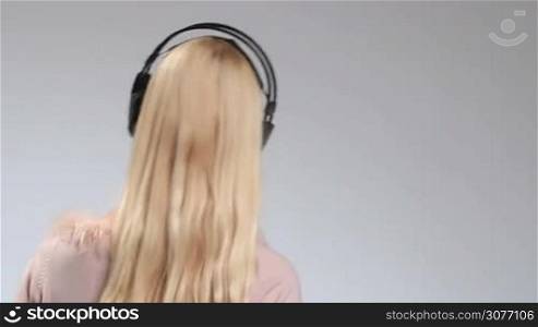 Emotional young woman in big headphones listening to her favorite song on the radio and making dance moves, back view on white. Bright positive teenage girl turning back and smiling at the camera while enjoying music in earphones.